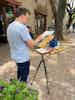 An artist paints a plaza scene on a portable easel.