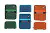 Three colors of empty Pocket Art Toolkits (green, blue, and orange) are sitting on a table, each shown open and closed.