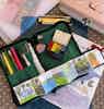 Open toolkit and palette and other sketching supplies lay splayed out, with an open zigzag book af a camping trip.